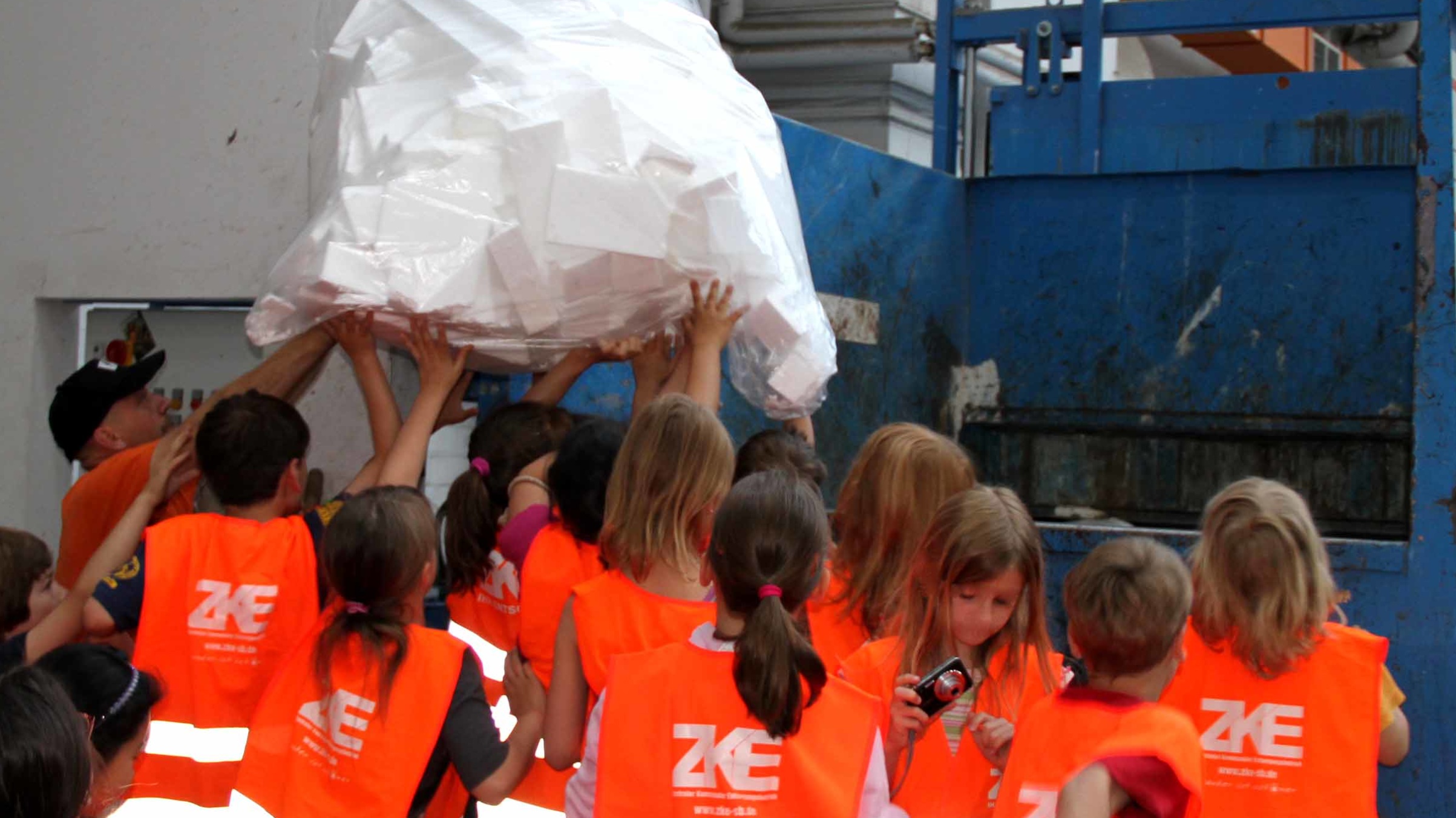 Kinder heben gemeinsam Müll in einen Container